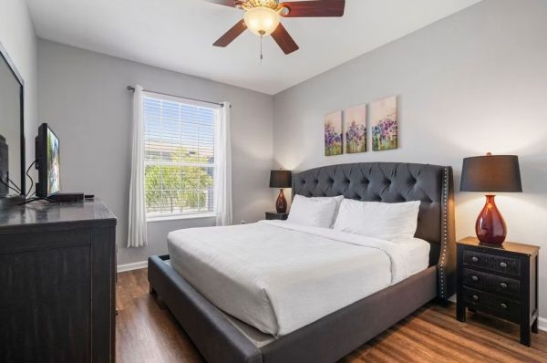 Bedroom with a gray tufted bed, white bedding, two black nightstands with lamps, and a ceiling fan.